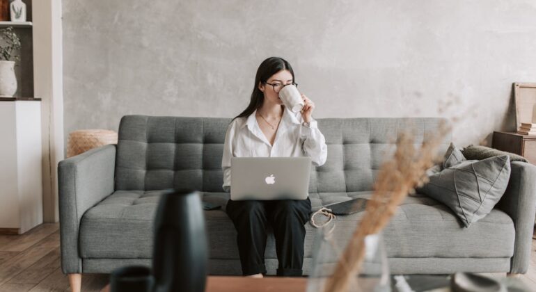 woman drinking coffee with a laptop sitting on the sofa