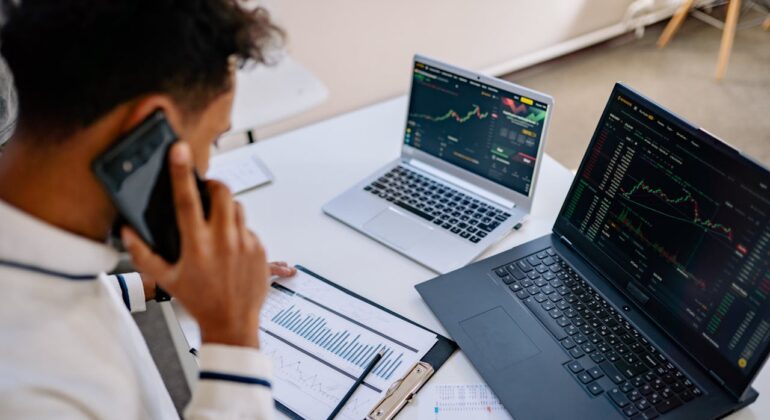 man checking graphs on a laptop with a phone on his hand