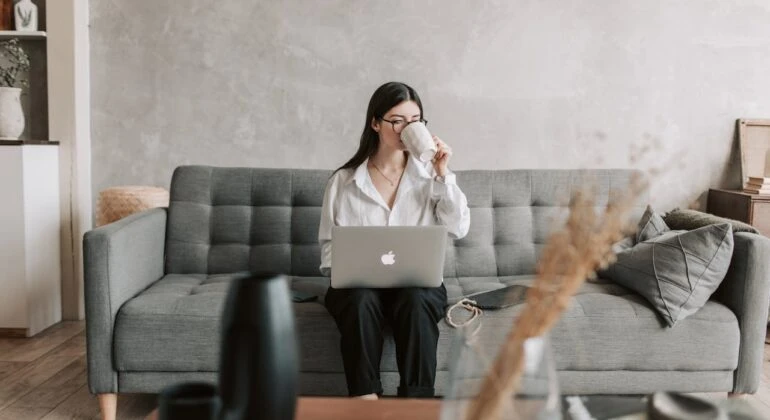 woman drinking coffee with a laptop sitting on the sofa