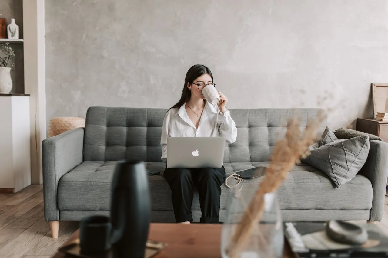 woman drinking coffee with a laptop sitting on the sofa